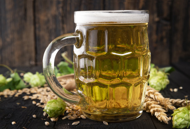 啤酒杯与绿色啤酒花和小麦在木制黑色背景图片下载