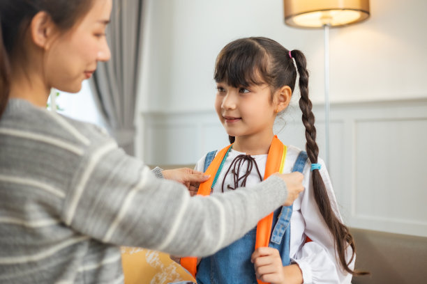 亚洲母亲帮助女儿背着书包准备上学。图片下载