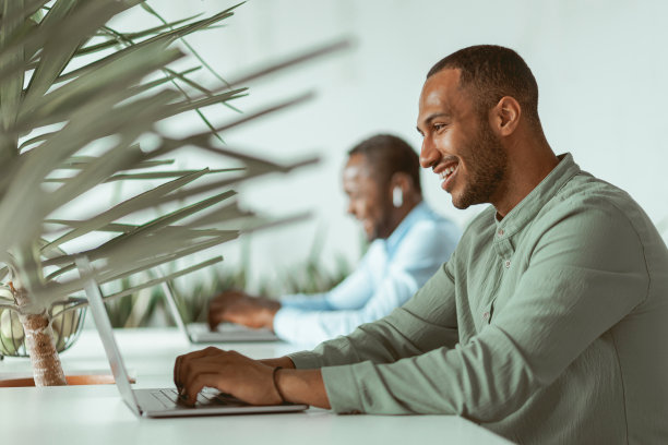 英俊的非洲商人在笔记本电脑上工作，坐在同事背景下工作图片下载