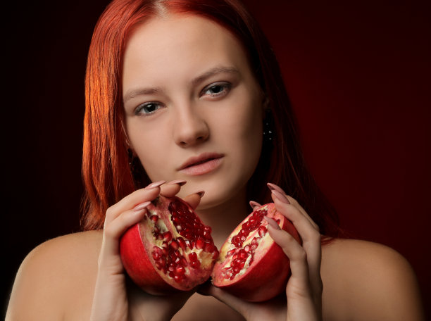 红色背景上一个红头发和石榴水果的年轻女孩的肖像图片下载