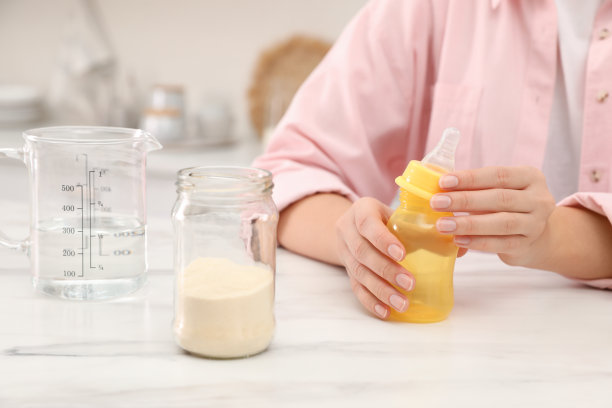 妇女在室内的桌子上准备婴儿配方奶粉，特写。婴儿奶粉图片下载