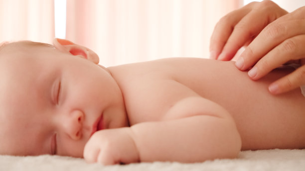 母亲正在给她健康熟睡的婴儿按摩。小白种新生儿躺在他的肚子上休息，而他的母亲正在为他的小背部和发展中的肌肉进行按摩。图片下载