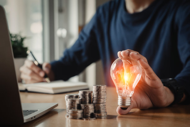 商人把灯泡放在桌上的硬币堆上，以实现节能省钱的理念。图片下载