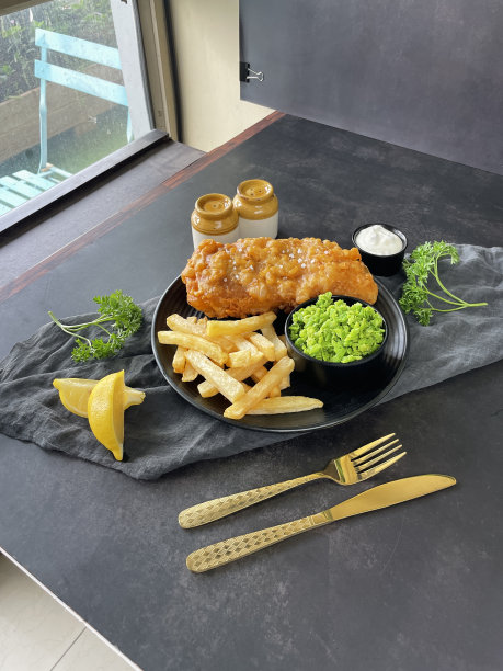 图片背后的美食摄影工作室的照片拍摄设置，在室内拍摄鱼，薯片和豌豆糊黑色盘子，香芹装饰，鞑靼酱，刀叉，cruet set，柠檬楔形，灰色薄纱，灰色背景图片下载