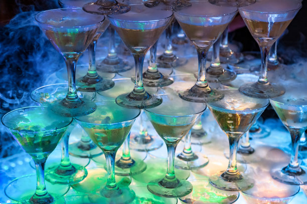 节日背景的酒杯与香槟金字塔，点燃灯光在正式的婚礼上。盛香槟的玻璃杯被建造成金字塔的形状。设计节日背景。复制文本空间图片下载