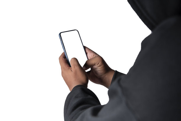 一名戴着面具、身穿黑色卫衣的匿名黑客展示了一款带有剪切路径的白屏智能手机。黑客和恶意软件的概念。图片下载