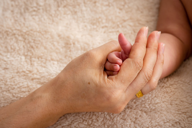 她在家里的床上舒服地睡觉时，充满爱意和关心地抱着可爱的宝宝的手指。刚出生的婴儿深睡在床上图片下载