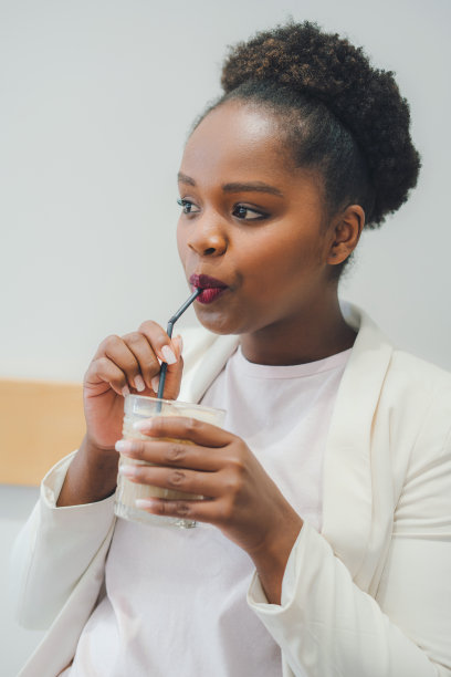 特写的非洲妇女坐在咖啡馆独自喝冰拿铁在夏天的晴天。饮料用玻璃杯喝。有用的拿铁咖啡。图片下载