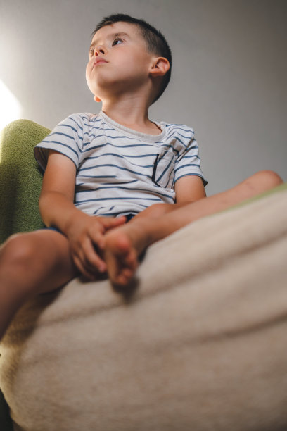 一个可爱的白人男孩坐在家里的沙发上，看着远处专心。教育休闲娱乐爱好活动。看电视屏幕。图片下载