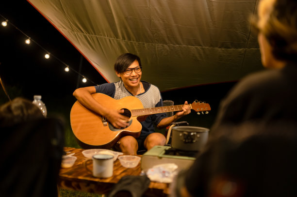 亚洲男子在野营气氛中弹吉他与家人坐在晚餐，弹吉他和玩得很开心图片下载