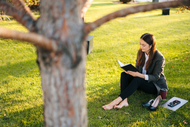 自由职业者女性坐在草地上记日记，写要做的清单。书，咖啡杯，铅笔，野草。年轻的商业女性思考图片下载