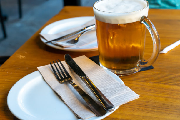 大啤酒杯放在两个盘子之间的桌子上图片下载