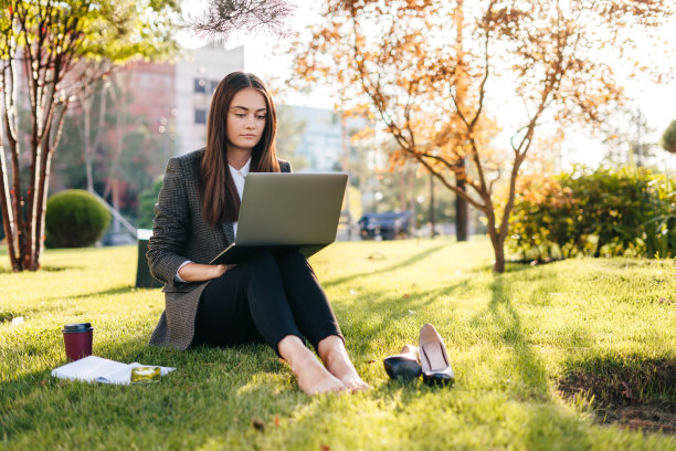 身着正装的女商人坐在夏日公园的草地上，用笔记本电脑远程工作。现代商业的概念。计算机技术的概念。商业，事业成功的概念。环境的概念。图片下载