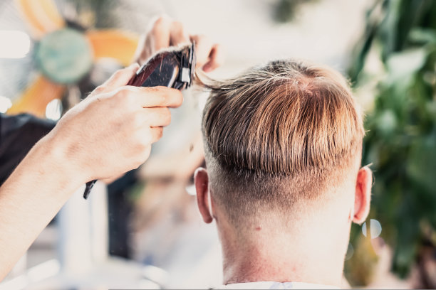 生活照片理发店。年轻的男顾客戴着口罩，侧面背部后视图。理发师男手工动梳子工具电动剪刀。现代短发。时尚服务沙龙图片下载