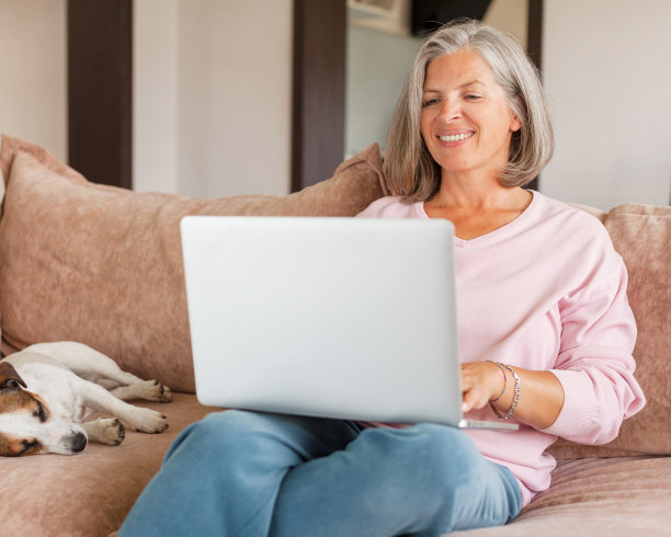 成熟女子坐在沙发上使用无线笔记本电脑应用程序浏览互联网图片下载