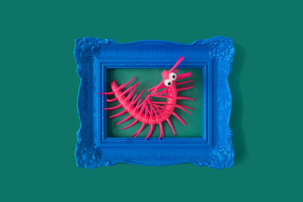 一只粉红色的塑料毛毛虫，大眼睛，在绿色背景的复古蓝色框架中。滑稽超现实的万圣节庆祝派对邀请或广告的概念图片下载