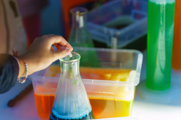 一个孩子的手把一块干冰扔进一个装有蓝色液体的烧瓶里图片下载