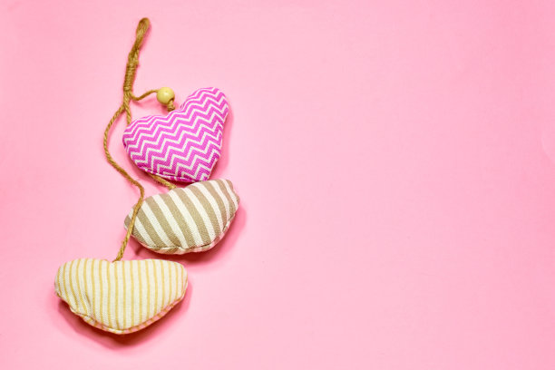 柔软的织物心形飞行在柔软的粉红色背景，复制空间。情人节概念设计图片下载