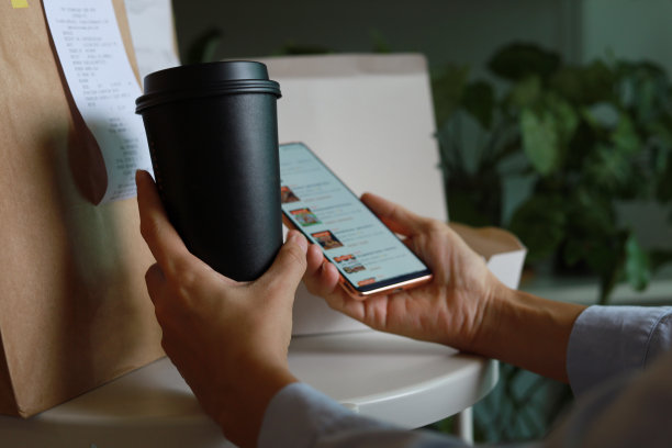 近距离拍摄的女性一边使用智能手机一边享受送货上门的饮料和食物图片下载