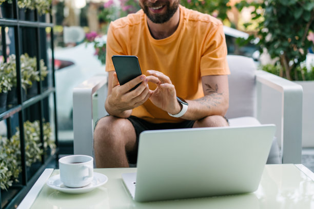 年轻英俊的男子坐在时髦的街头咖啡馆，喝着咖啡，用他的笔记本电脑和手机远程工作图片下载