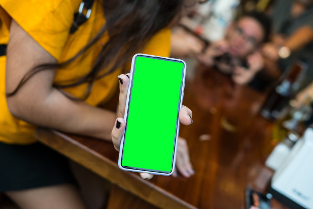 孩子们正在玩手机游戏背景，一个女孩展示手机与绿色屏幕水平照片聚焦在前景图片下载
