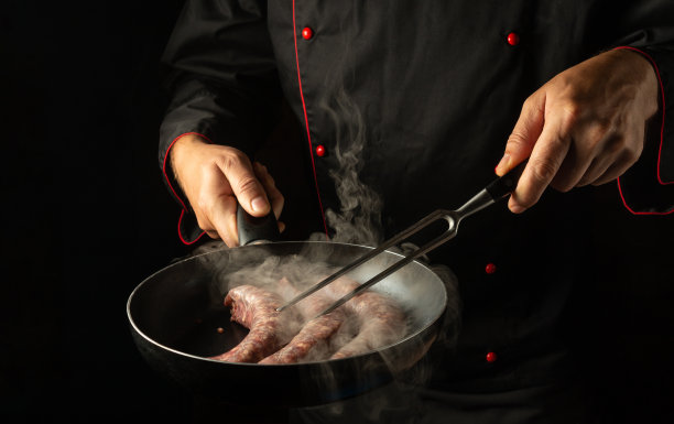 厨师用煎锅煎肉肠。放置酒店菜单在黑色背景图片下载