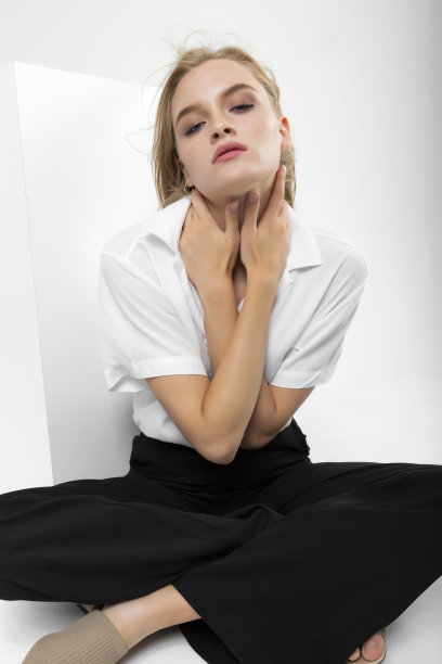 金发长发的女孩穿着白衬衫和黑色的布裤子在时尚拍摄。图片下载