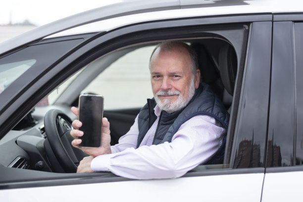 老年司机在汽车或出租车上的肖像，带着手机图片下载