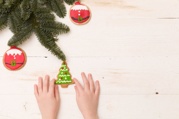 孩子的手拿自制的圣诞树饼干在白色的木制背景与云杉树枝和装饰。圣诞节,节日庆典。在家烘烤。图片下载