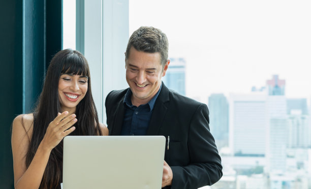 女商人和商人一起用笔记本电脑工作。男人和女人开心地笑着，看着笔记本。商务人士站在轻松的工作场所。现代办公环境下的同事团队工作图片下载