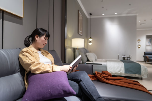 一位亚洲妇女正在她房间的沙发上看书图片下载