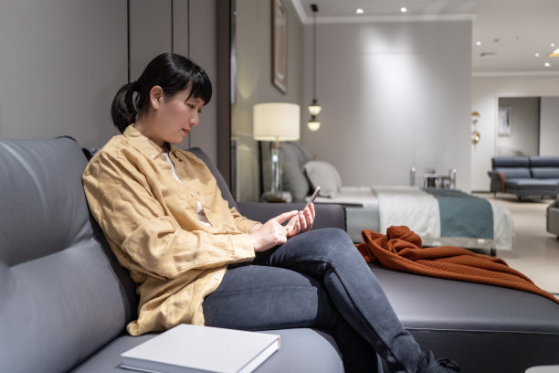 一位亚洲家庭主妇坐在沙发上用手机图片下载