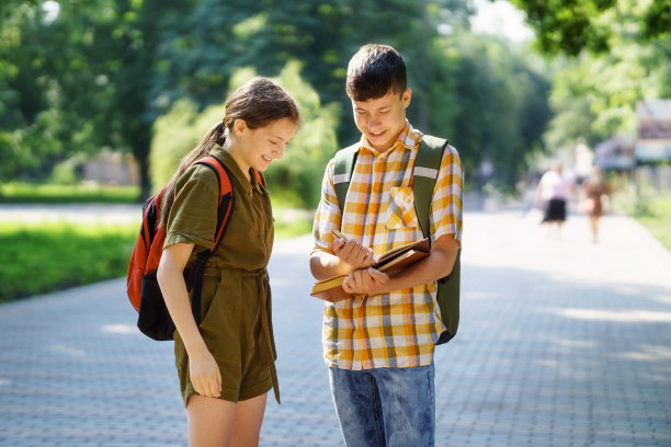 城市公园里的学生画像，十几岁的小学生一个男孩和一个女孩正站在小路上讨论功课，读书和聊天图片下载