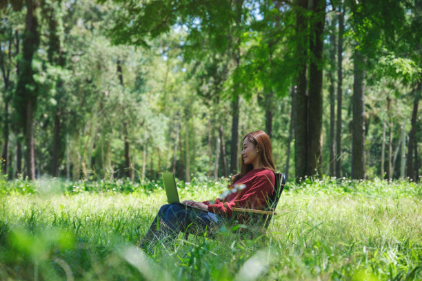一位美丽的亚洲妇女坐在公园的椅子上，在笔记本电脑键盘上打字图片下载