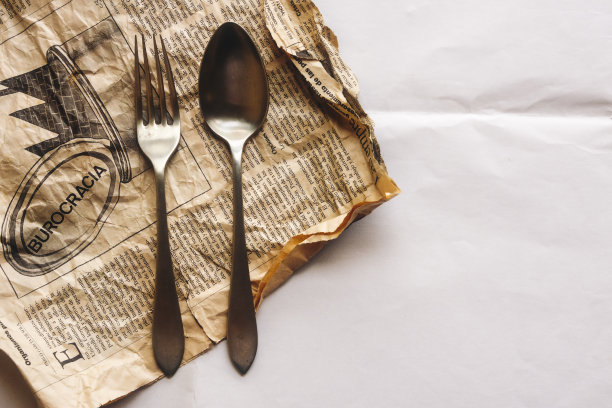 一把勺子和一把叉子放在一张旧报纸上，上面用西班牙语写着“官僚主义”这个词，在报纸的右边有一个版面图片下载