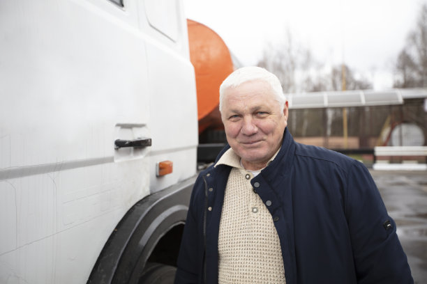 一位上了年纪的司机坐在一辆大卡车的驾驶室旁。图片下载