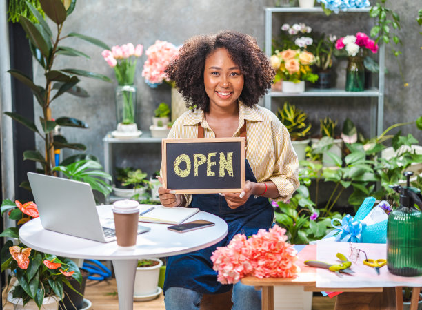 非裔美国女性影响力或中小企业所有者微笑工作在家庭摄像机自拍。面带微笑的女花商打电话。年轻女子在花店工作与开放的标志..图片下载