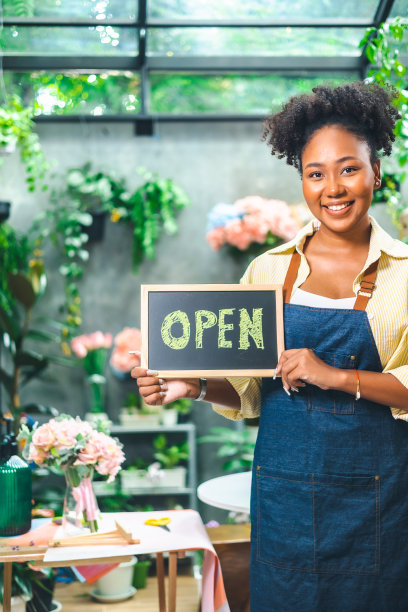非裔美国女性影响力或中小企业所有者微笑工作在家庭摄像机自拍。面带微笑的女花商打电话。年轻女子在花店工作与开放的标志..图片下载