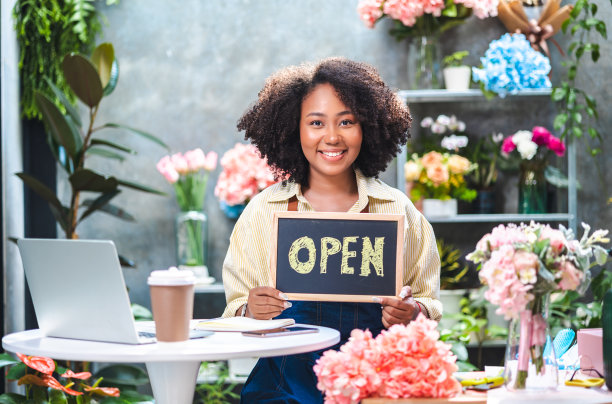 非裔美国女性影响力或中小企业所有者微笑工作在家庭摄像机自拍。面带微笑的女花商打电话。年轻女子在花店工作与开放的标志..图片下载