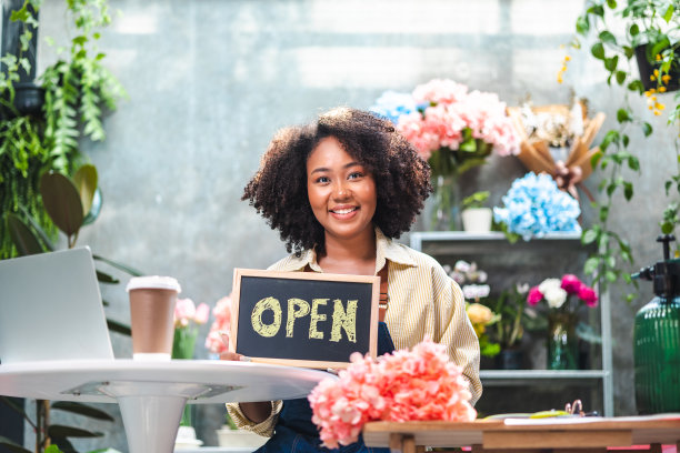 非裔美国女性影响力或中小企业所有者微笑工作在家庭摄像机自拍。面带微笑的女花商打电话。年轻女子在花店工作与开放的标志..图片下载