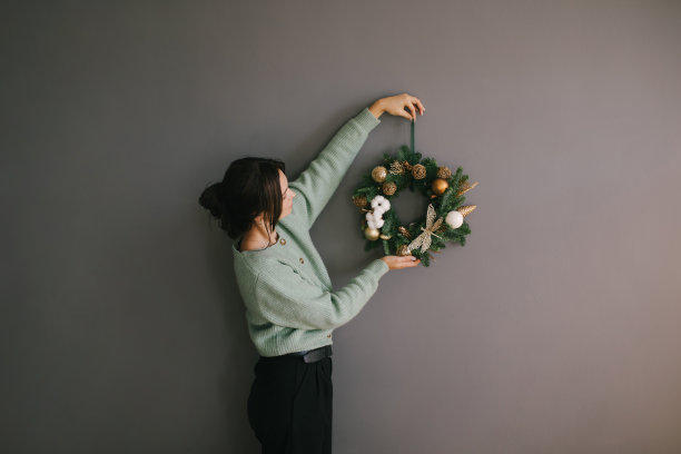 千禧一代的女性用手工制作的圣诞花环装饰灰色的墙壁。喜庆的节日装饰。图片下载