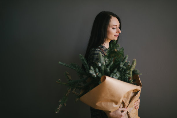 千禧年妇女拿着一大束松枝包在牛皮纸，准备做圣诞花环和节日装饰图片下载