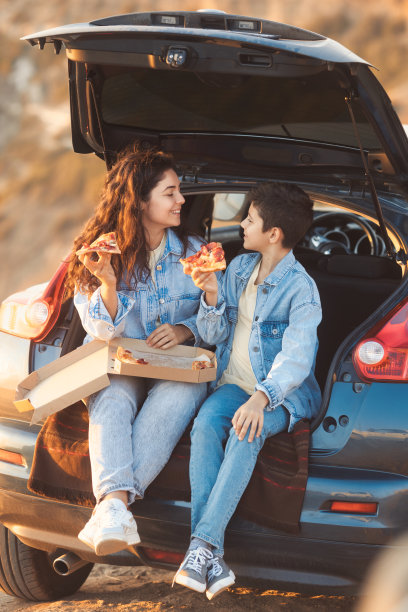 垂直全身全家福的姐姐和她十几岁的弟弟坐在车里玩，一起吃披萨图片下载