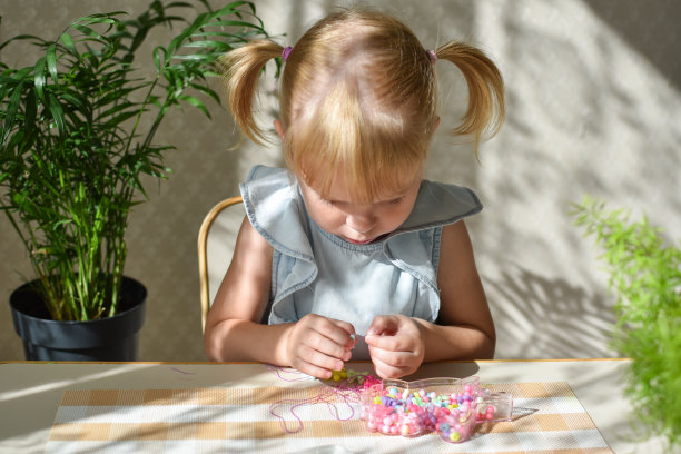一个两岁的小女孩正坐着收集小珠子。儿童精细运动技能的发展DIY。图片下载