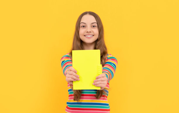 快乐的孩子微笑着展示学校课本为复制空间的黄色背景，知识图片下载