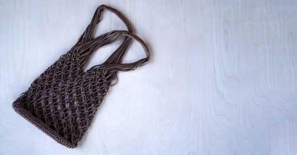 棕色绳袋编织在流苏技术从针织绳在木制背景。平铺，俯视图。零浪费和无塑料概念。你的文字，广告的地方。图片下载