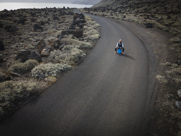 穿着西装的男人完全绝望地坐在那里，被击倒在一个蓝色的汽油罐上，在世界尽头的火山沙漠的某个地方图片下载