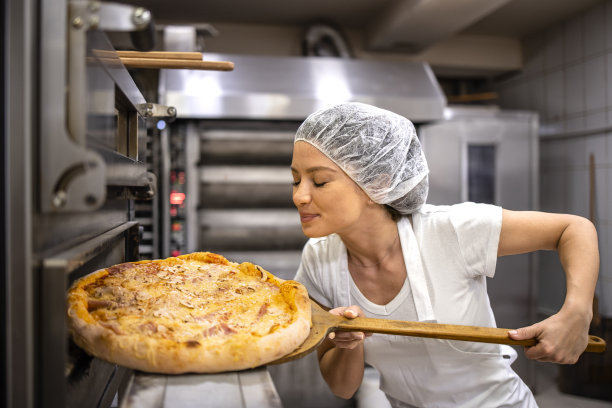 女餐厅厨师喜欢从披萨店厨房的烤箱里新鲜出炉的披萨的味道。图片下载