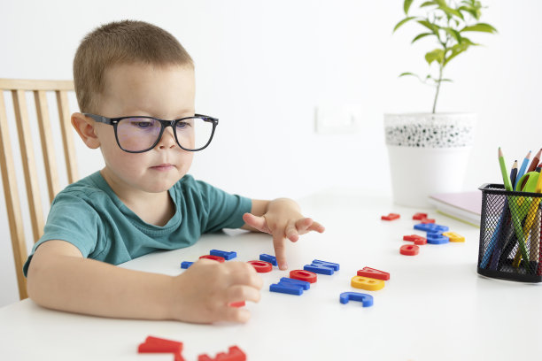 一个戴着眼镜坐在白桌子旁的孩子使字母显得光彩夺目。图片下载