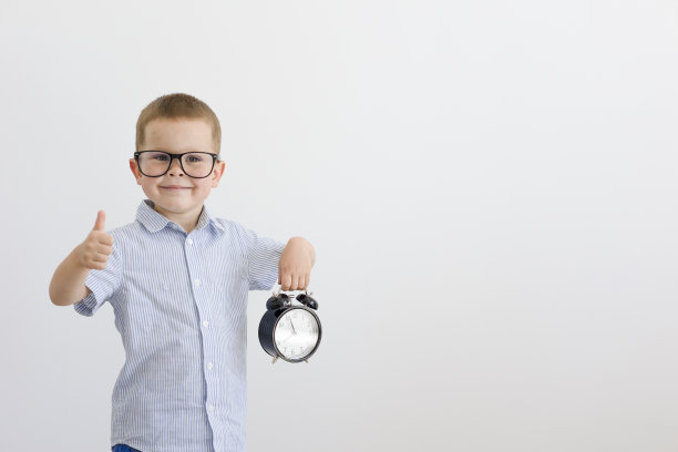 一个穿着蓝色衬衫的孩子微笑着，手里拿着一个闹钟。图片下载